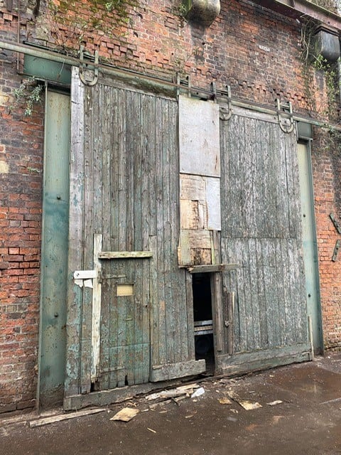 An old wooden sliding door, with panels missing and pieces breaking off. This door was replaced by a new roller shutter.